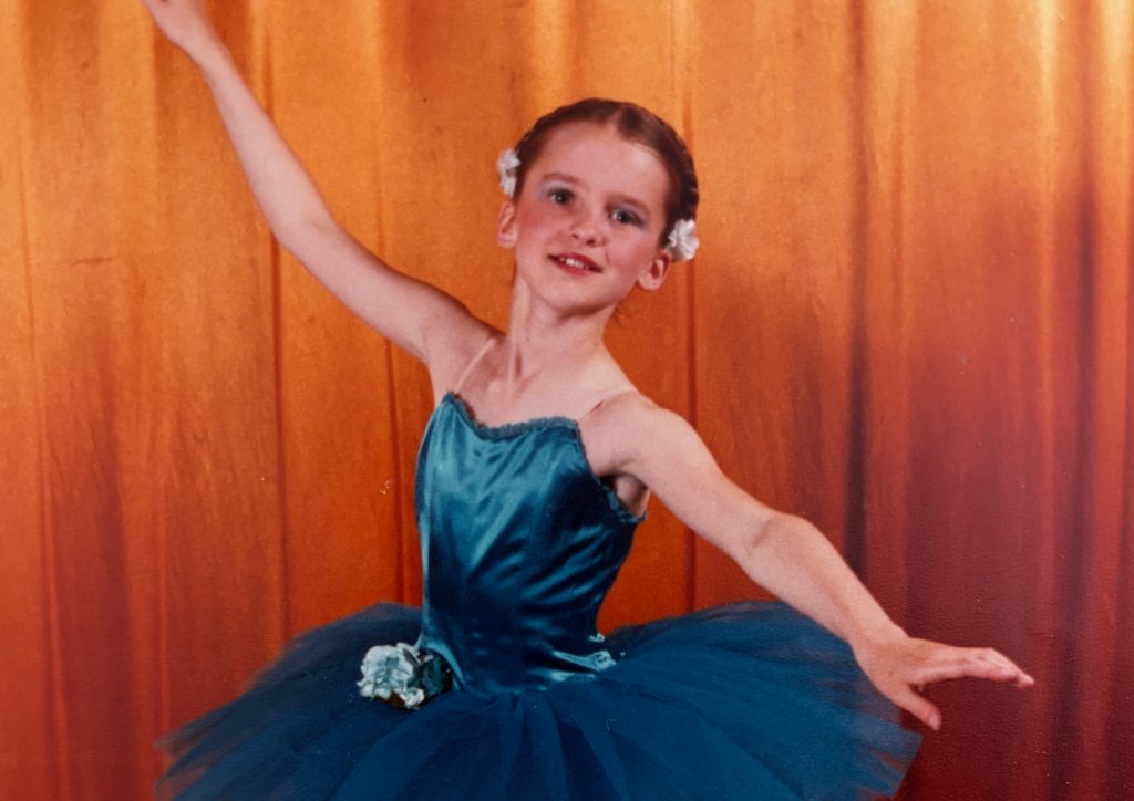 Cecily Salt aged 9 in a ballet pose wearing a shiny blue tutu against a golden curtain