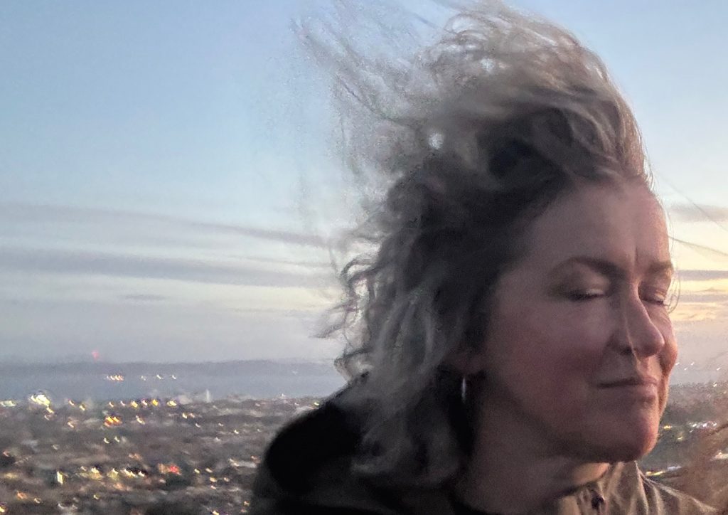 Cecily Salt with the wind blowing her hair up in the air, on a hill in Edinburgh at sunset